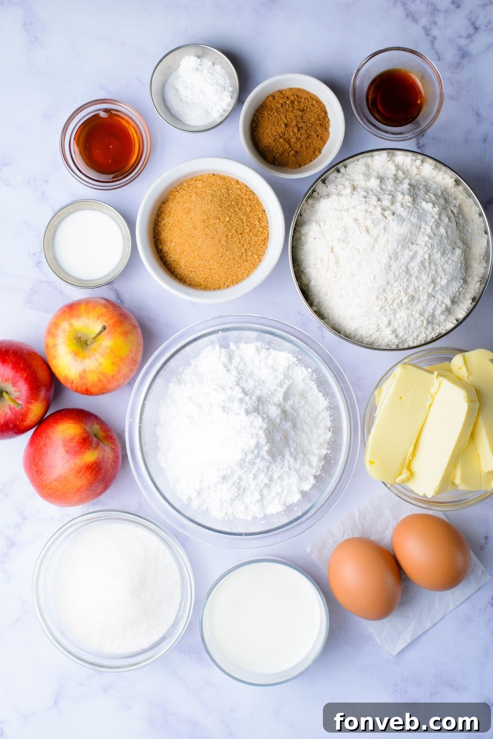Quick Glazed Apple Cinnamon Loaf 6 All the fresh ingredients for Apple Cinnamon Loaf Cake, neatly arranged in small glass bowls on a marble counter, including whole apples and eggs.