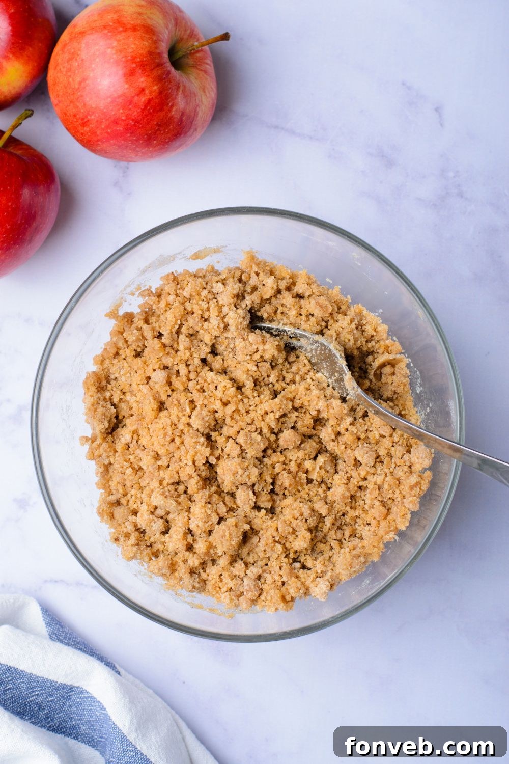 Quick Glazed Apple Cinnamon Loaf 10 A glass bowl holds a rich cinnamon sugar mixture, perfectly prepped for the crumb topping, with two fresh apples placed on the side on a light-colored table.