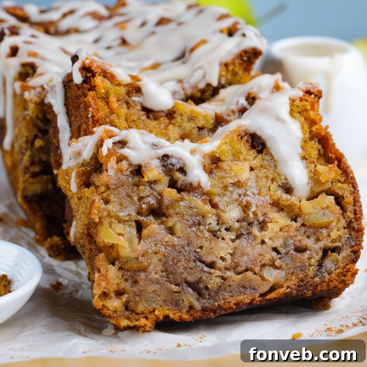 Amish Apple Fritter Bread sliced and placed on a parchment paper on table with a bowl with glaze to the side 
