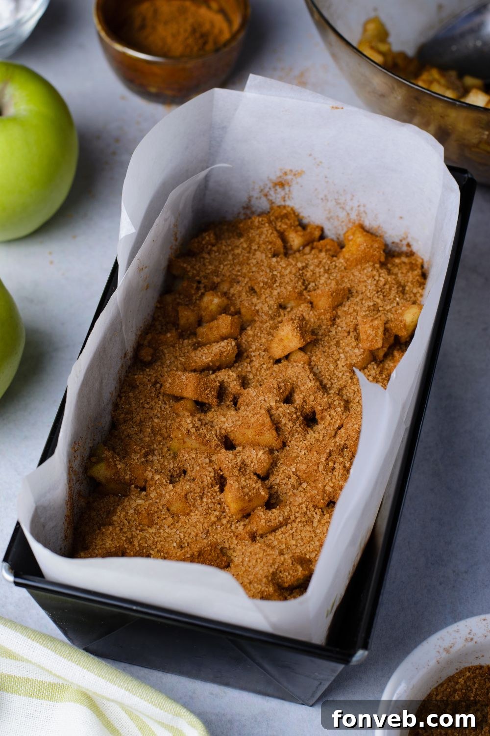 cinnamon mixture and diced apples inside a loaf pan sitting on marble table with green apples to side of pan 