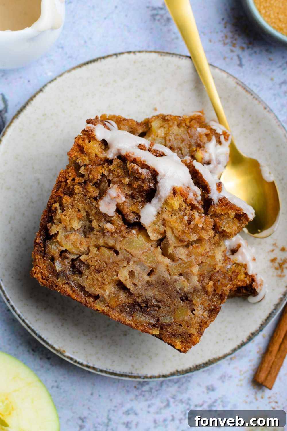 two slices of Amish Apple Fritter Bread on plate with a spoon to side of plate with a few bites taken out sitting on blue table 