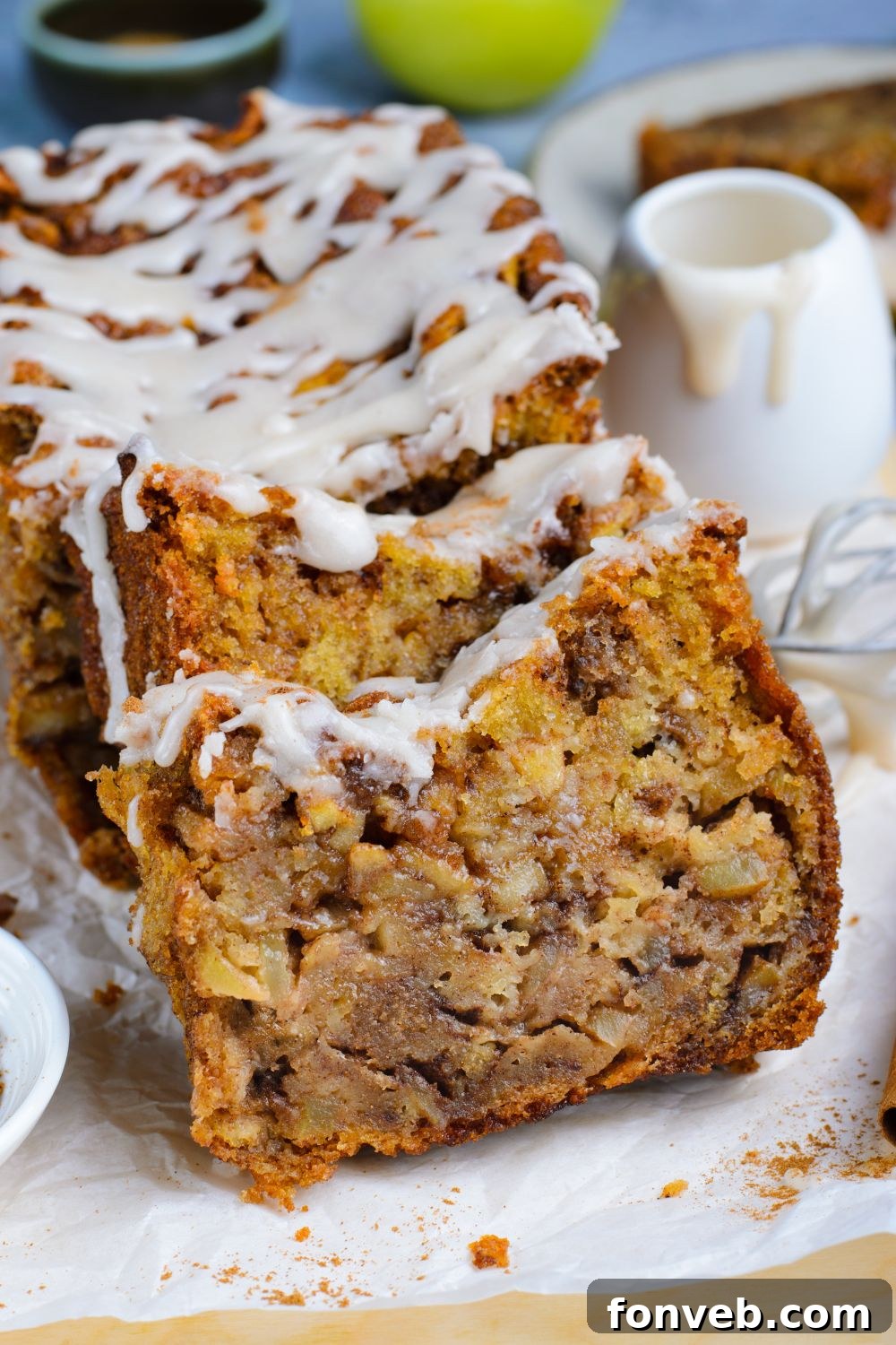 sliced Amish Apple Fritter Bread sitting on parchment paper on a wooden table with a sweet glaze drizzled on top 