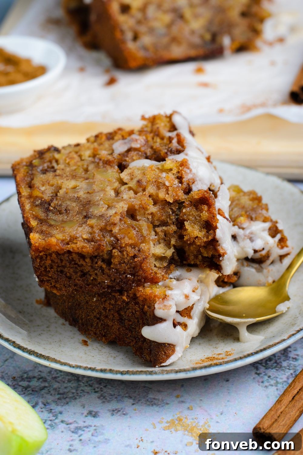 two slices of Amish Apple Fritter Bread  on a white plate with a gold spoon to side showing a couple bites taken out of it 