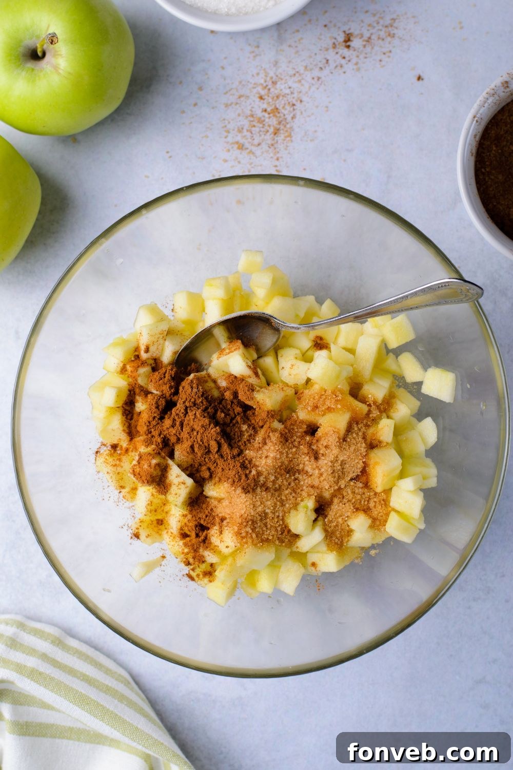 fresh diced apples in a bowl with some cinnamon on top and a spoon in bowl to mix 