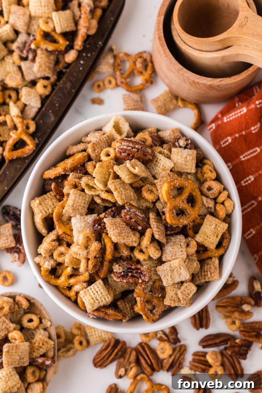 Pumpkin Spice Chex Mix scattered around a table with a bowl full of snack mix, and a sheet pan off to the side