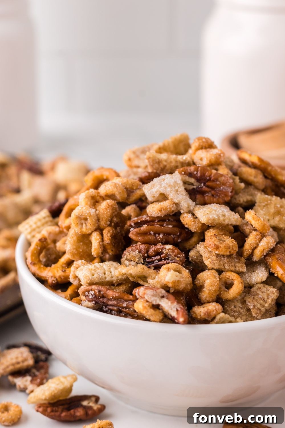 Pumpkin Spice Chex Mix scattered around on table and overflowing in a white bowl sitting on a marble counter