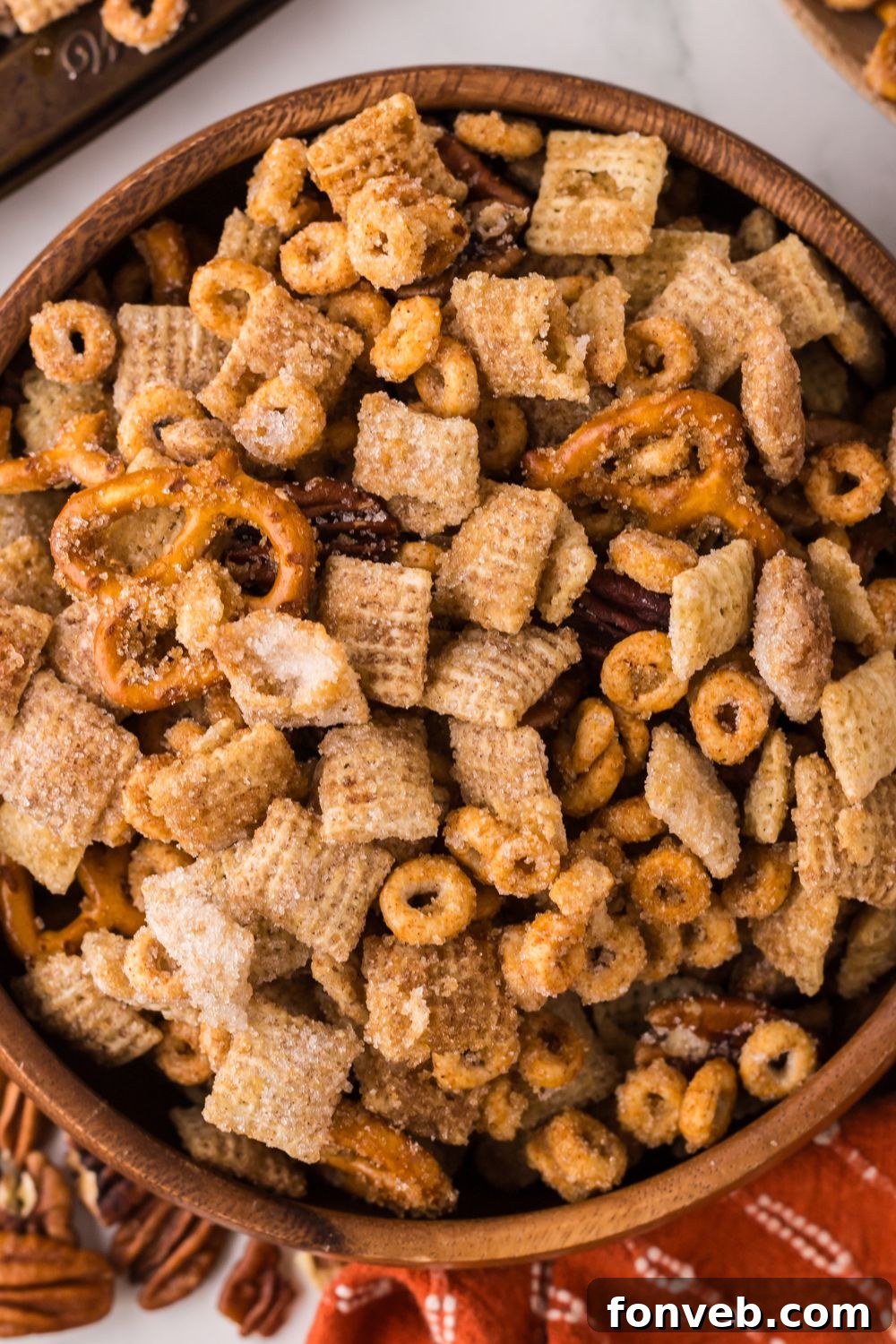 Pumpkin Spice Chex Mix in a wooden bowl and more around table and a towel under the bowl 