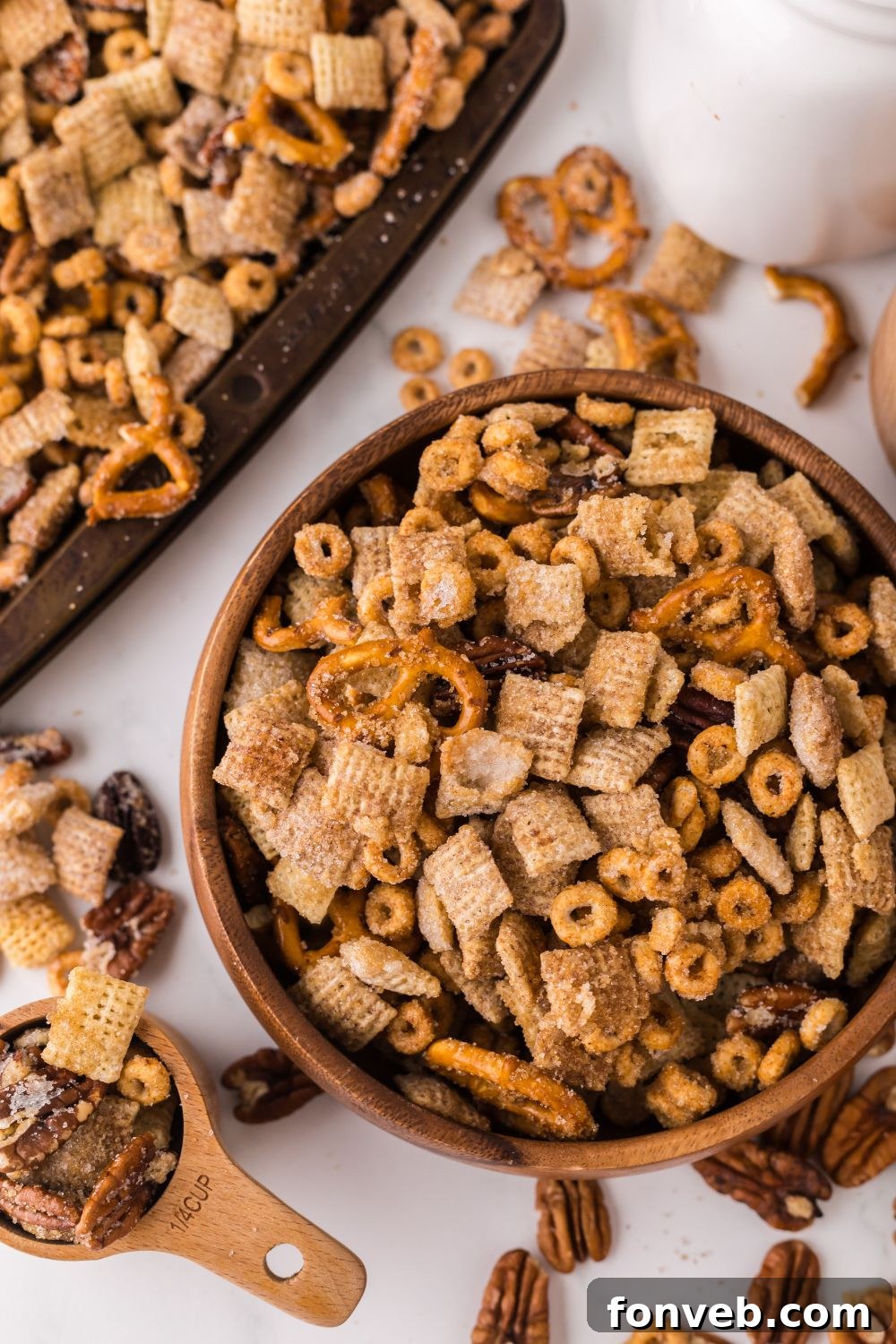 Pumpkin Spice Chex Mix in a wooden bowl and a measuring cup and sheet pan full of pumpkin snack mix