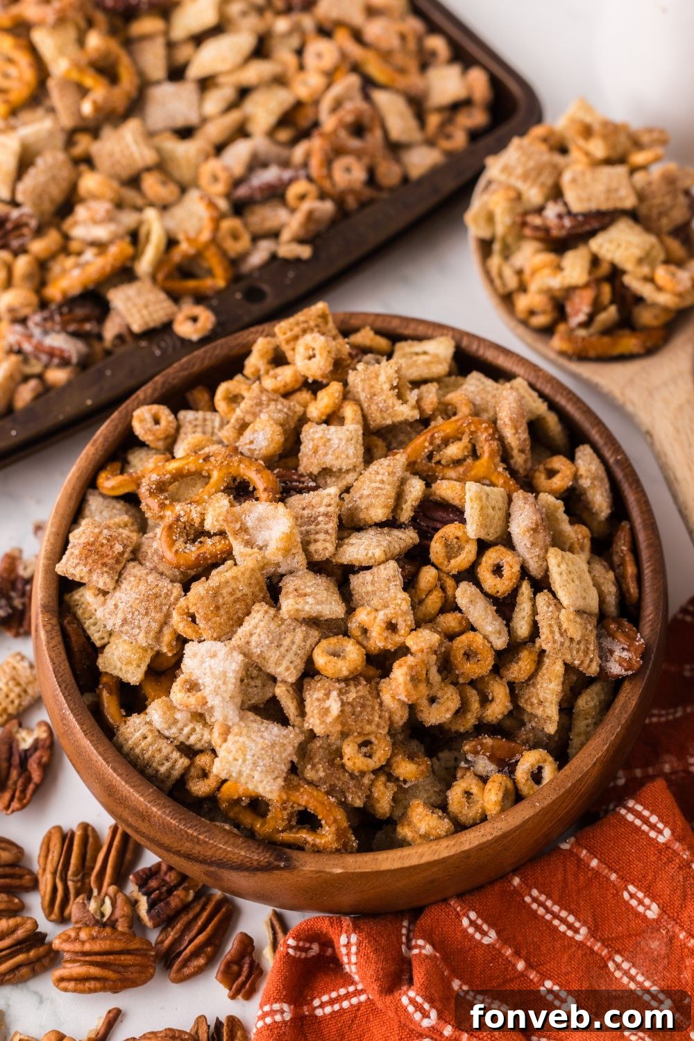 wooden bowl full of Pumpkin Spice Chex Mix and a sheet pan behind it with more of the snack mix
