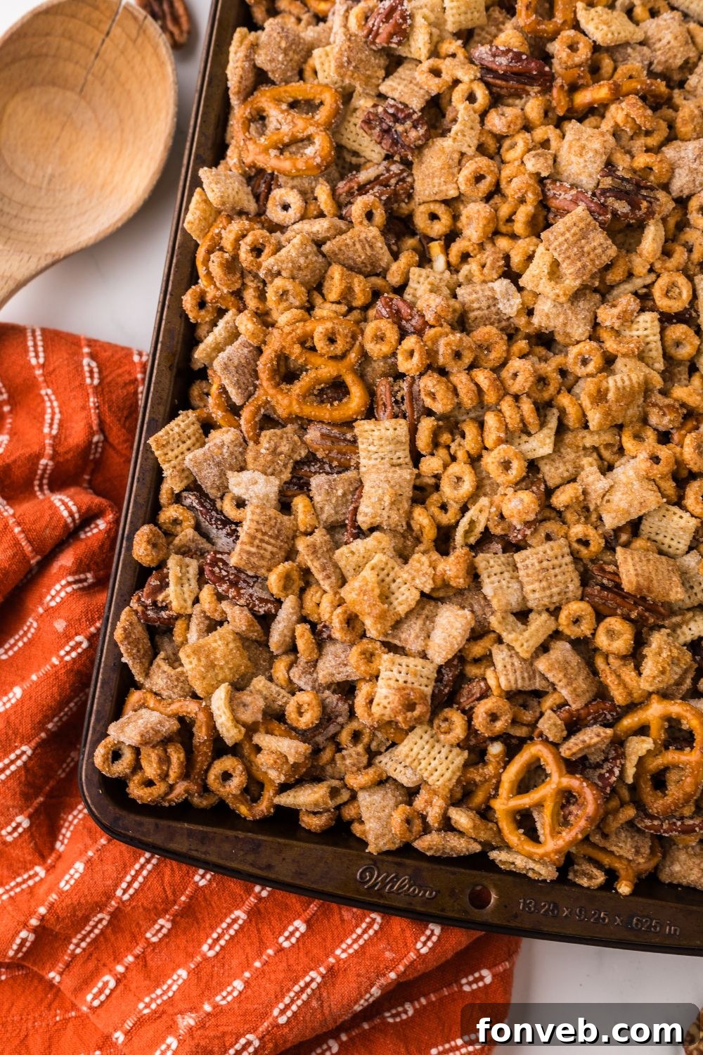 Pumpkin Spice Chex Mix spread out over a sheet pan with an orange striped towel on marble counter 