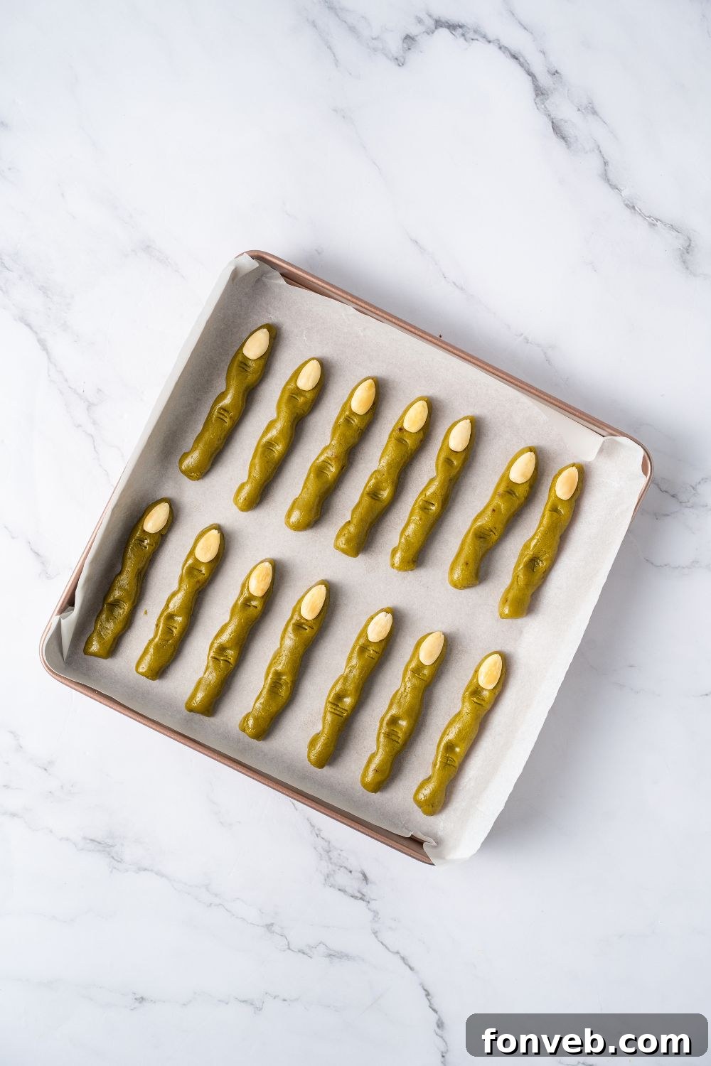 Witch Finger Cookies A Ghoulishly Fun Halloween Bake 13 raw pistachio Witch Finger Cookies on a parchment paper lined tray with almonds for finger nails