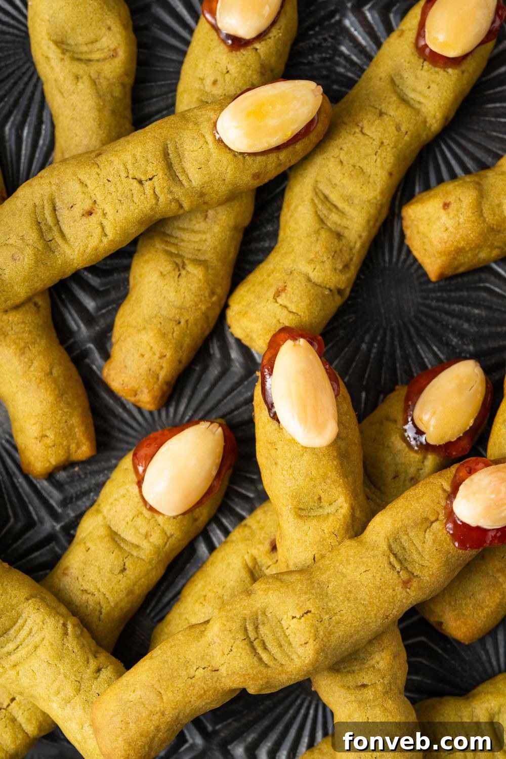 Witch Finger Cookies A Ghoulishly Fun Halloween Bake 4 Witch Finger Cookies on a black tray. The cookies are scattered around the tray