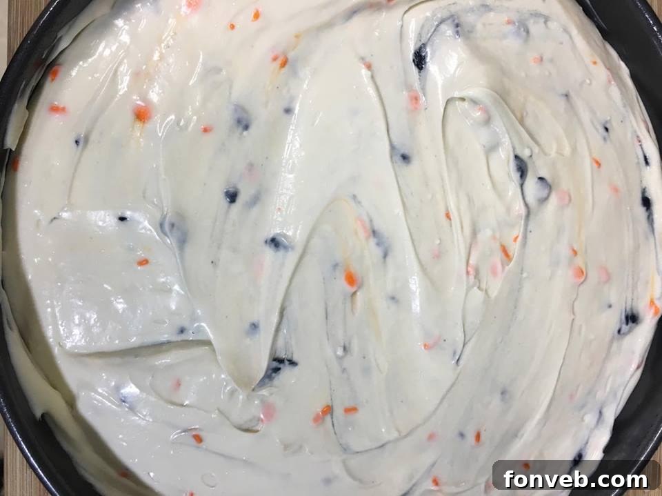 A close-up of a generous slice of Halloween Funfetti Cheesecake with a fluffy whipped topping