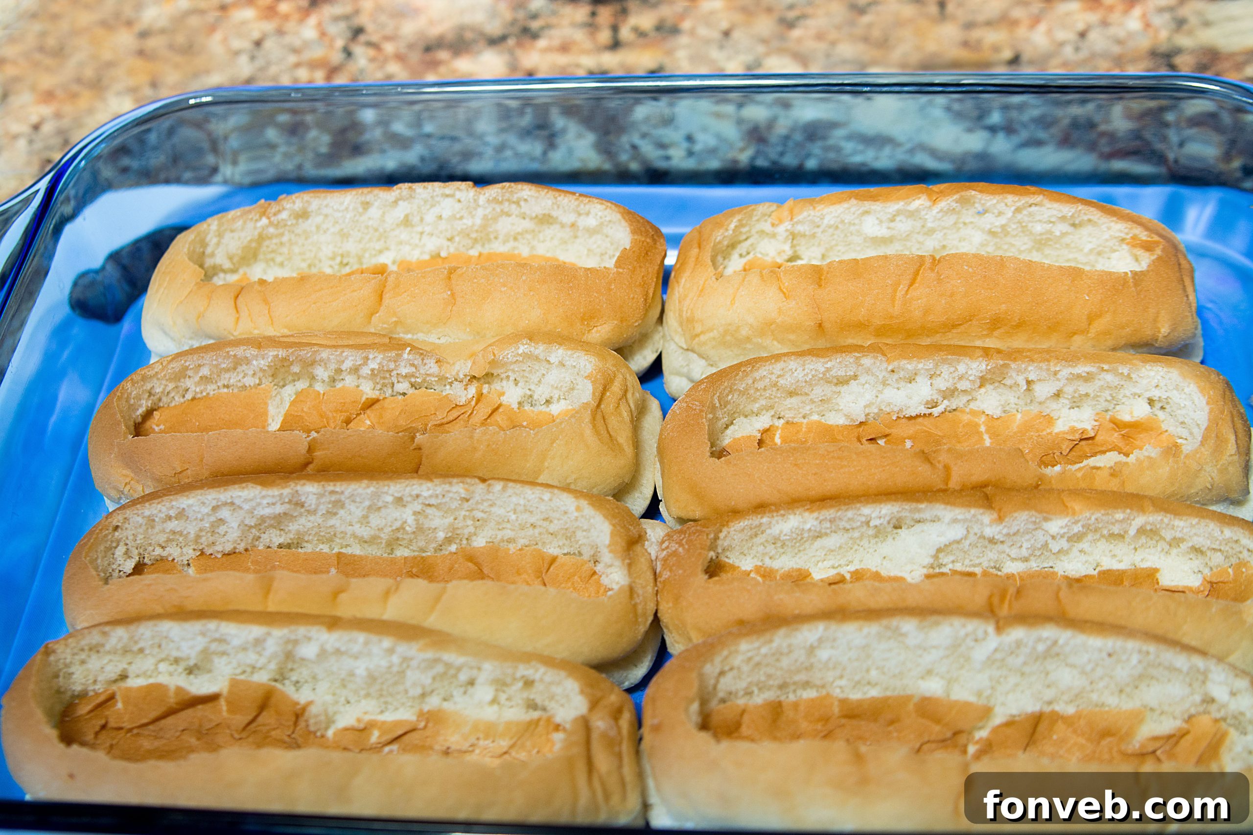 A knife carefully making an incision in a hot dog bun, showing the first step in creating the boat shape.