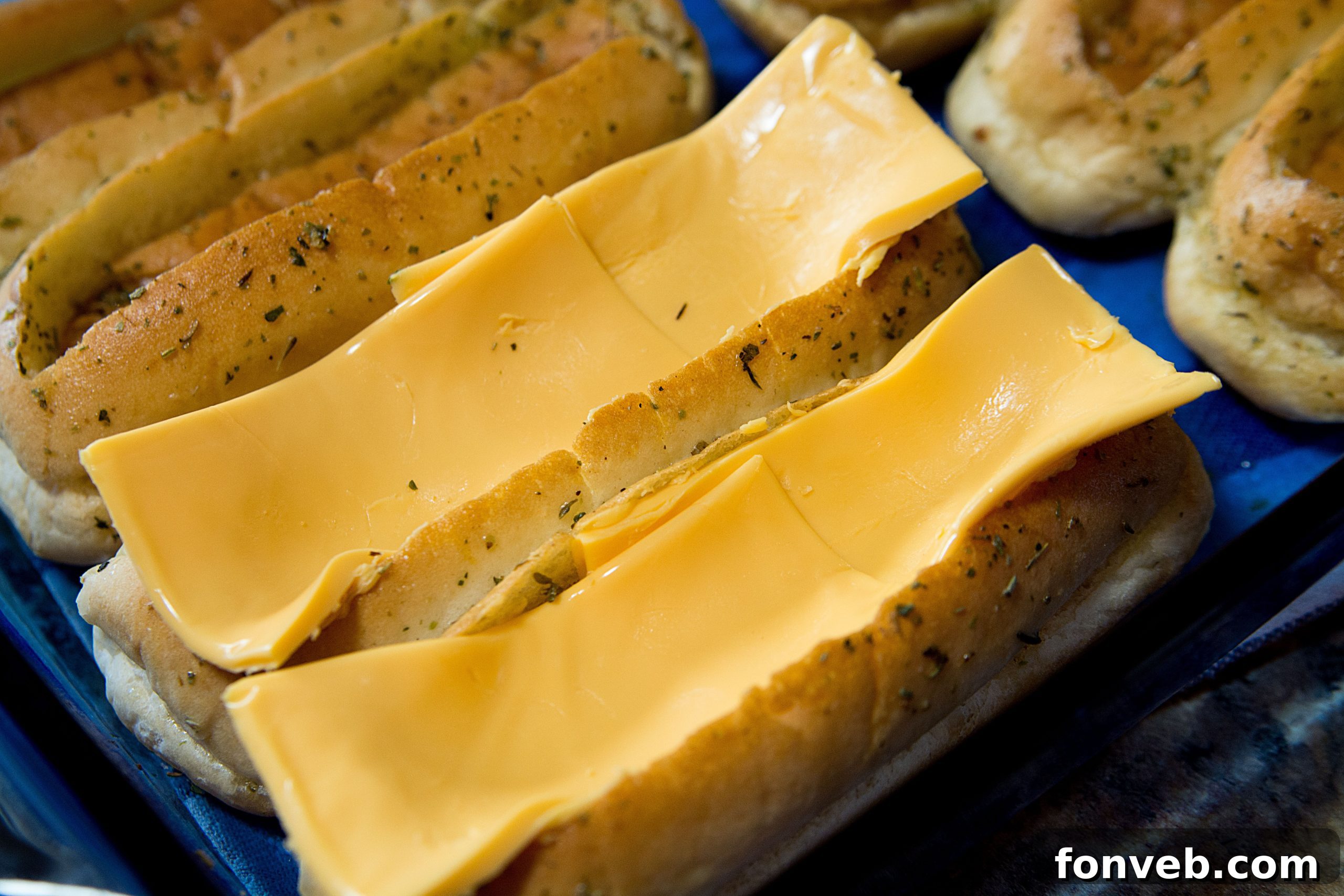 A hand brushing the savory garlic butter mixture onto the prepared hot dog buns in the baking dish.