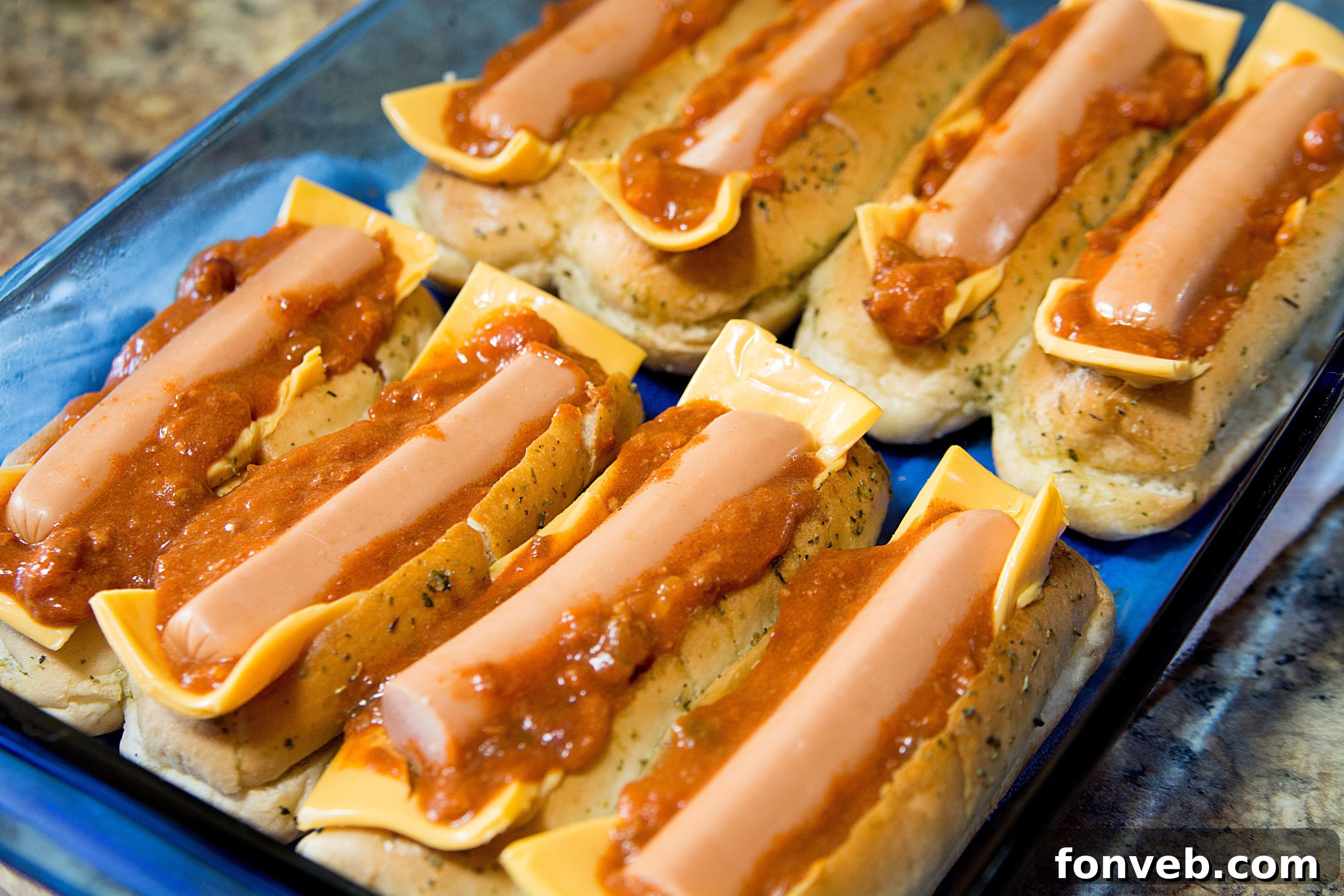 Hot dogs nestled in the buns, topped with chili and diced onions, before the final bake.