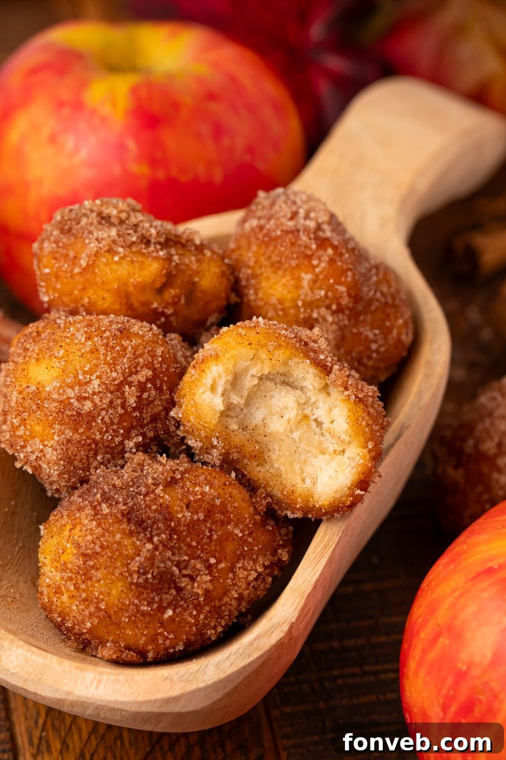 Apple Pie Donut Holes  in a wooden spoon on table with some apples beside the spoon 
