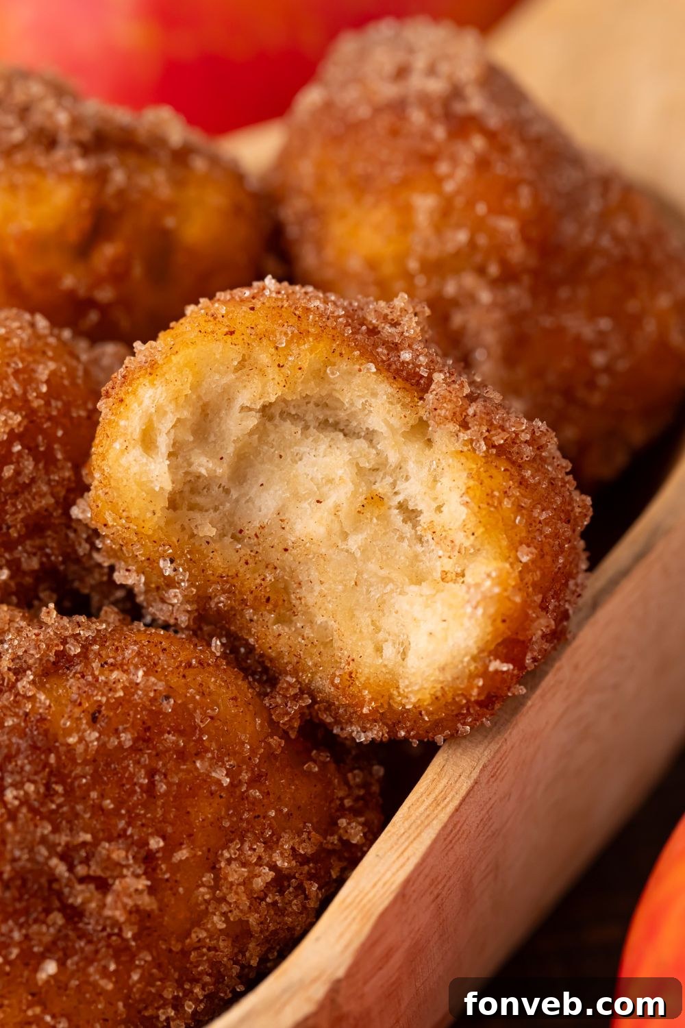 Apple Pie Donut Holes in a wooden spoon with one with a bite taken out of it sitting on top 