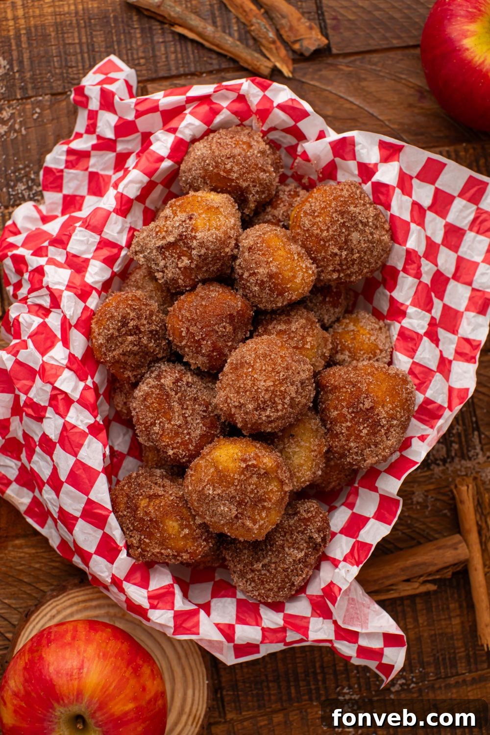 looking down on a wooden table with a basket full of Apple Pie Donut Holes and whole apples and cinnamon sticks around table 