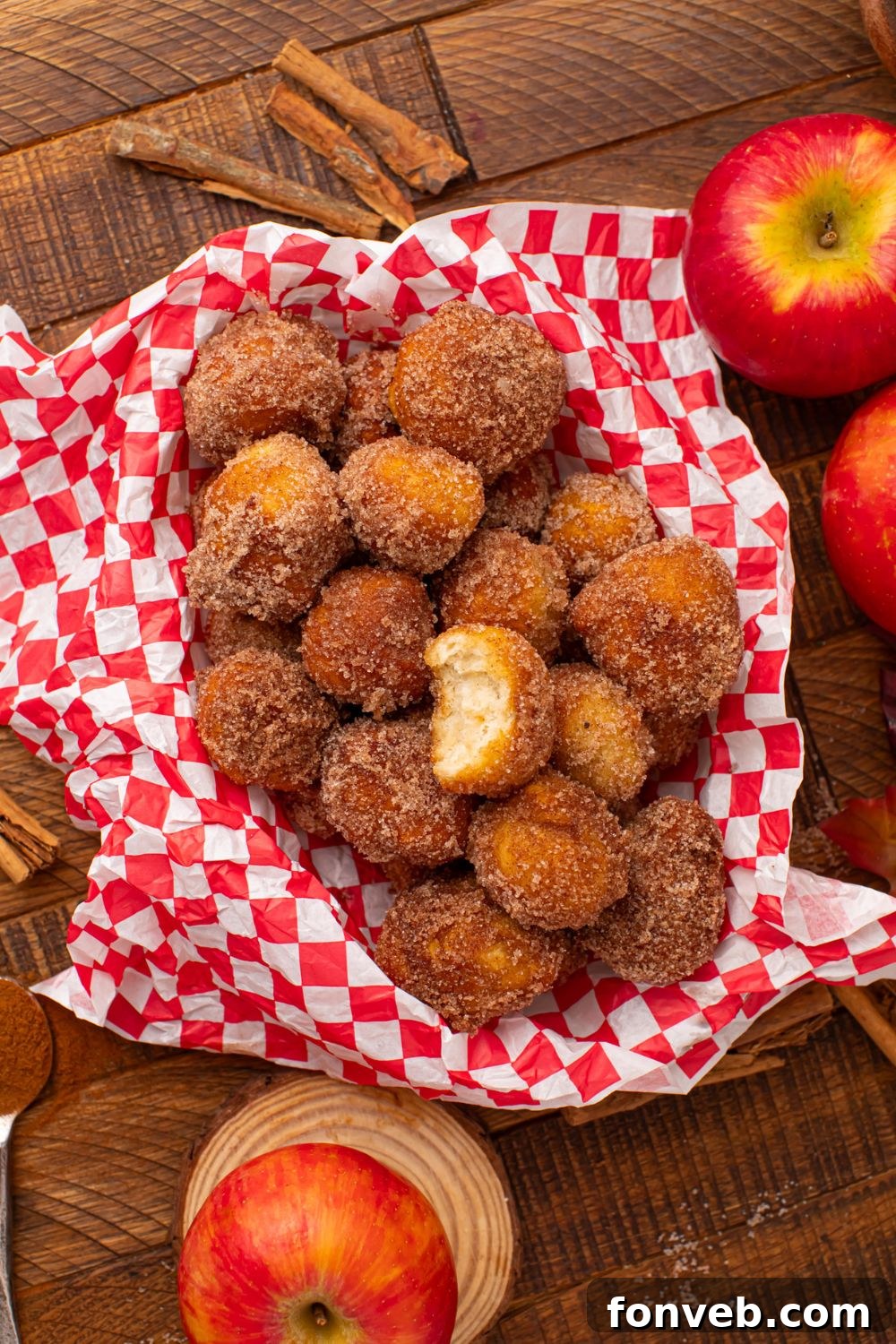 looking down at a wooden table with apples, cinnamon sticks and basket full of Apple Pie Donut Holes in the center