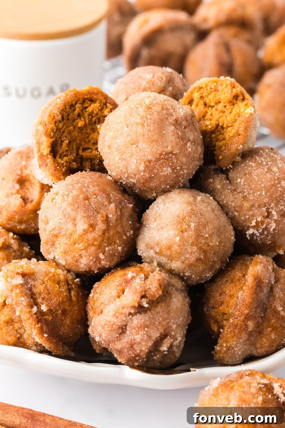 Cinnamon Sugar Baked Pumpkin Spice Donut Holes 11 Pumpkin Spice Donut Holes stacked on a plate with a few cut in half to show the centers of the donuts
