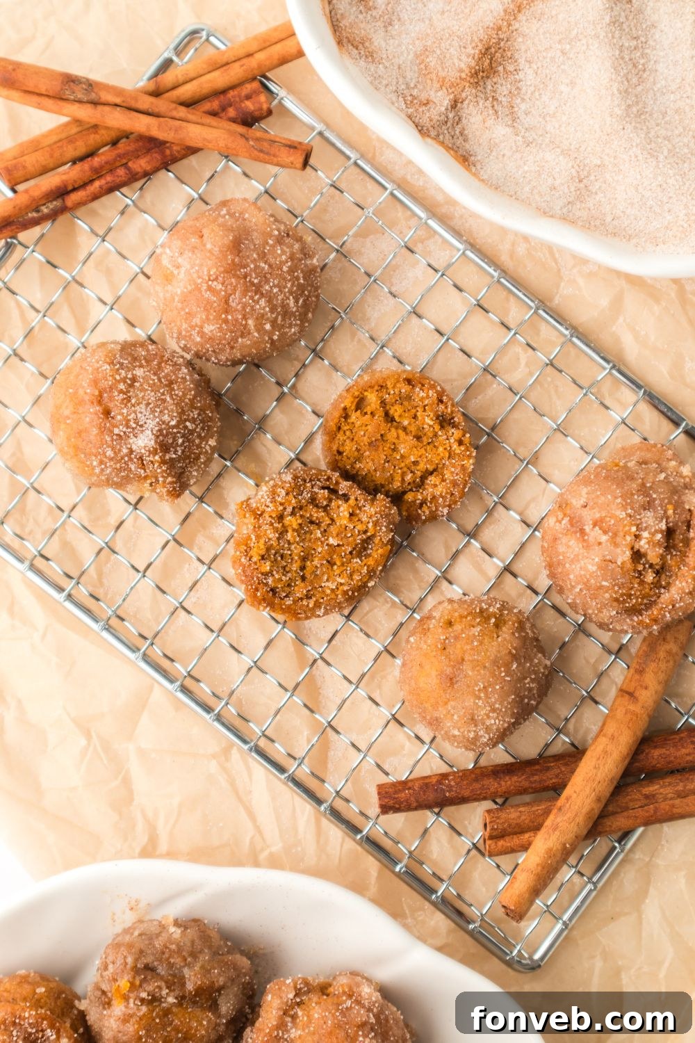 Cinnamon Sugar Baked Pumpkin Spice Donut Holes 12 Pumpkin Spice Donut Holes on a cooling rack with cinnamon sticks around the edges of the rack
