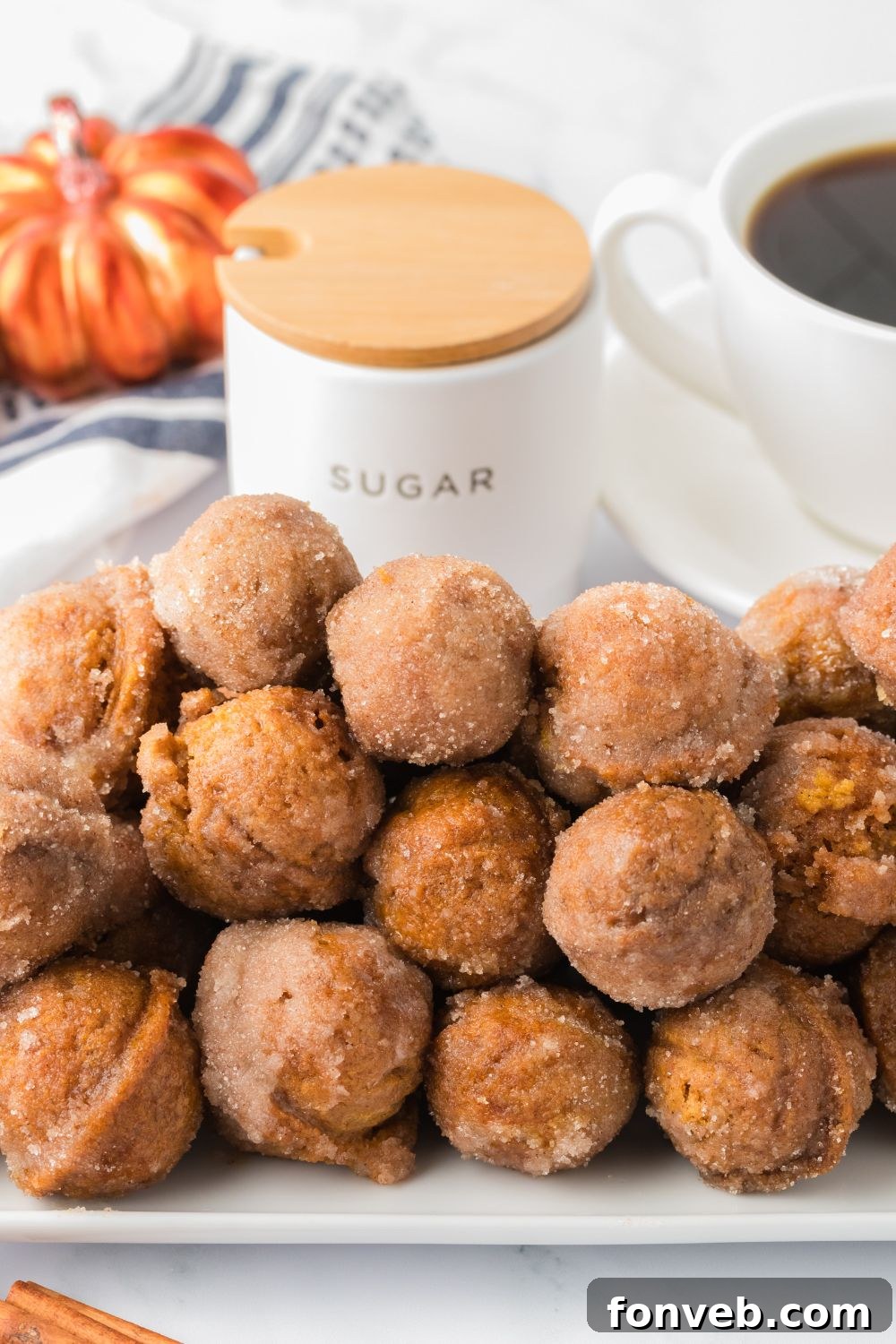 Cinnamon Sugar Baked Pumpkin Spice Donut Holes 22 white rectangle chair on table stacked with pumpkin donut holes, and a cup of coffee and fall decor behind it on the table