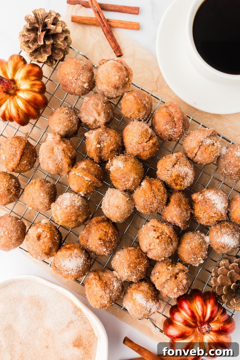 Cinnamon Sugar Baked Pumpkin Spice Donut Holes 17 Pumpkin Spice Donut Holes scattered on a cooling rack on table with a faux pumpkin to side