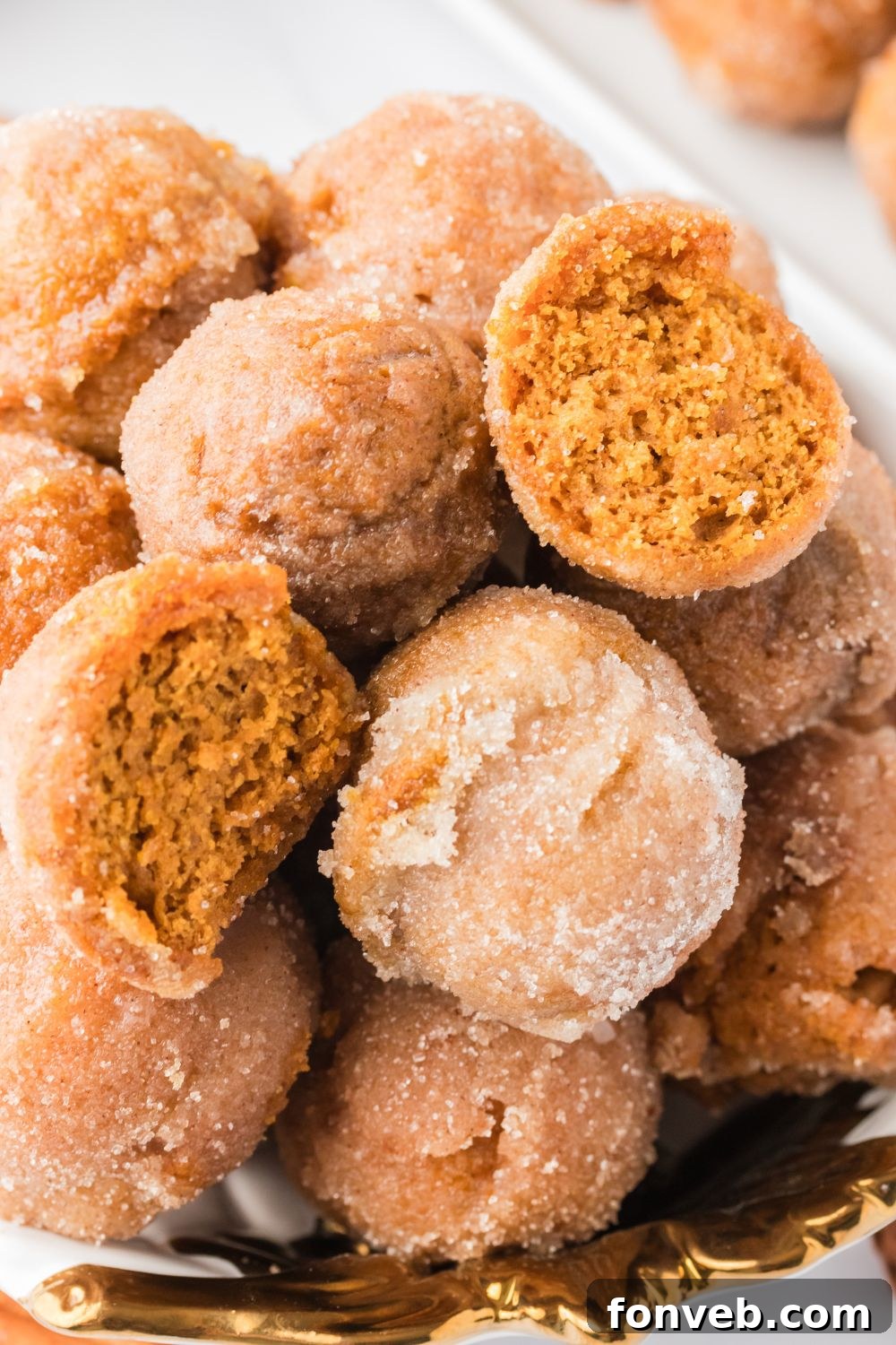 Cinnamon Sugar Baked Pumpkin Spice Donut Holes 3 Pumpkin Spice Donut Holes stacked on a platter with one cut in half to see the fluffy center of the donut holes