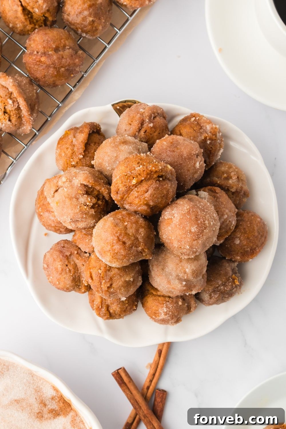 Cinnamon Sugar Baked Pumpkin Spice Donut Holes 19 Pumpkin Spice Donut Holes on a white plate sitting on table with cinnamon sticks to side, and more donuts on tray in background