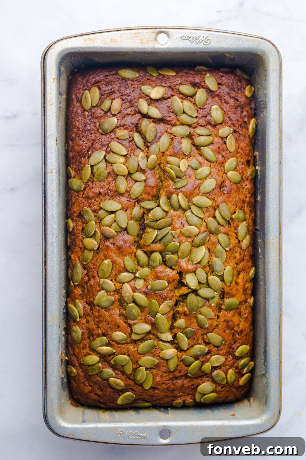 Starbucks Pumpkin Bread in a loaf pan on table with pumpkin seeds all over the top of bread 