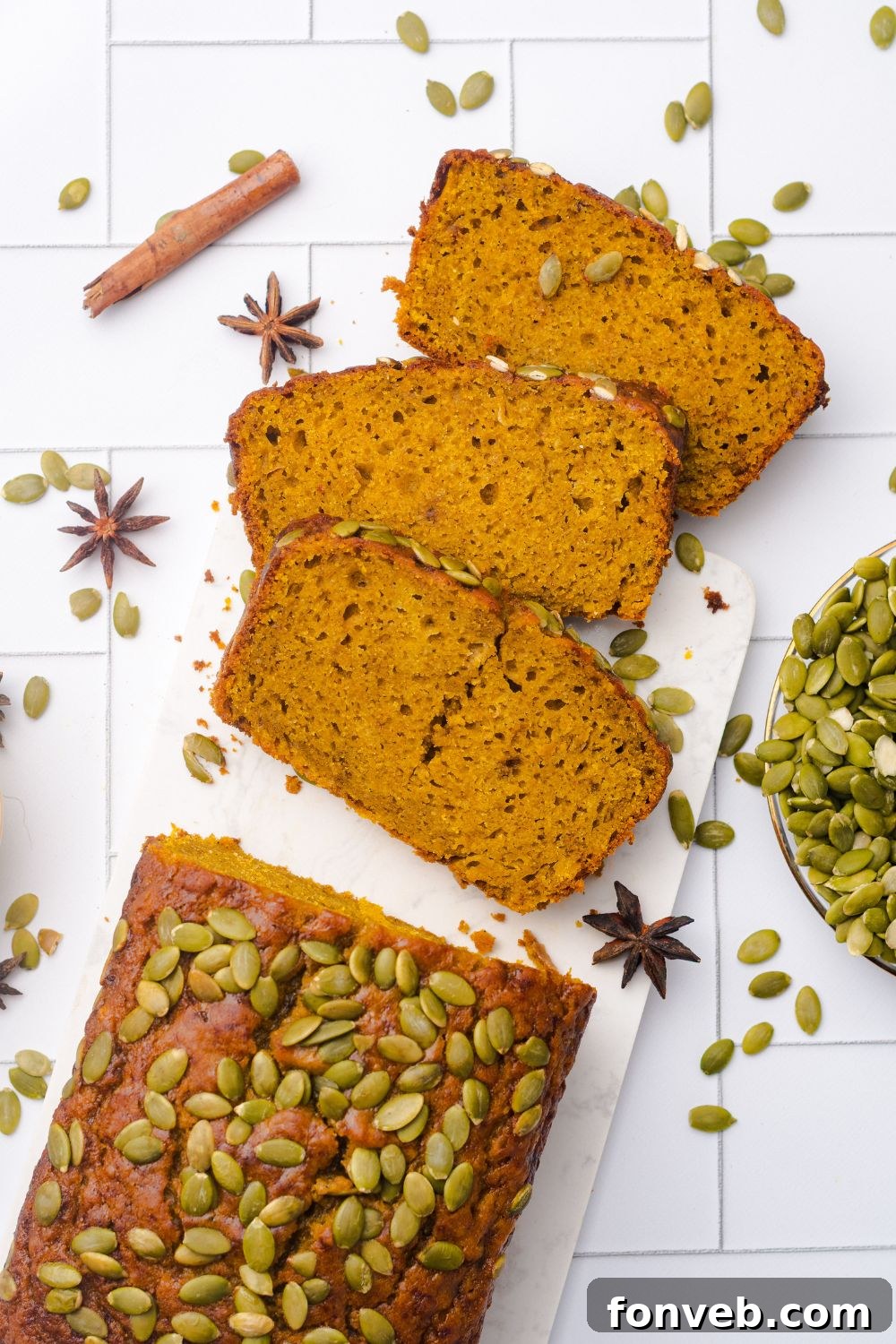 looking down on table to a loaf of Starbucks Pumpkin Bread with three slices placed on table with pumpkin seeds, and cinnamon sticks around the table 