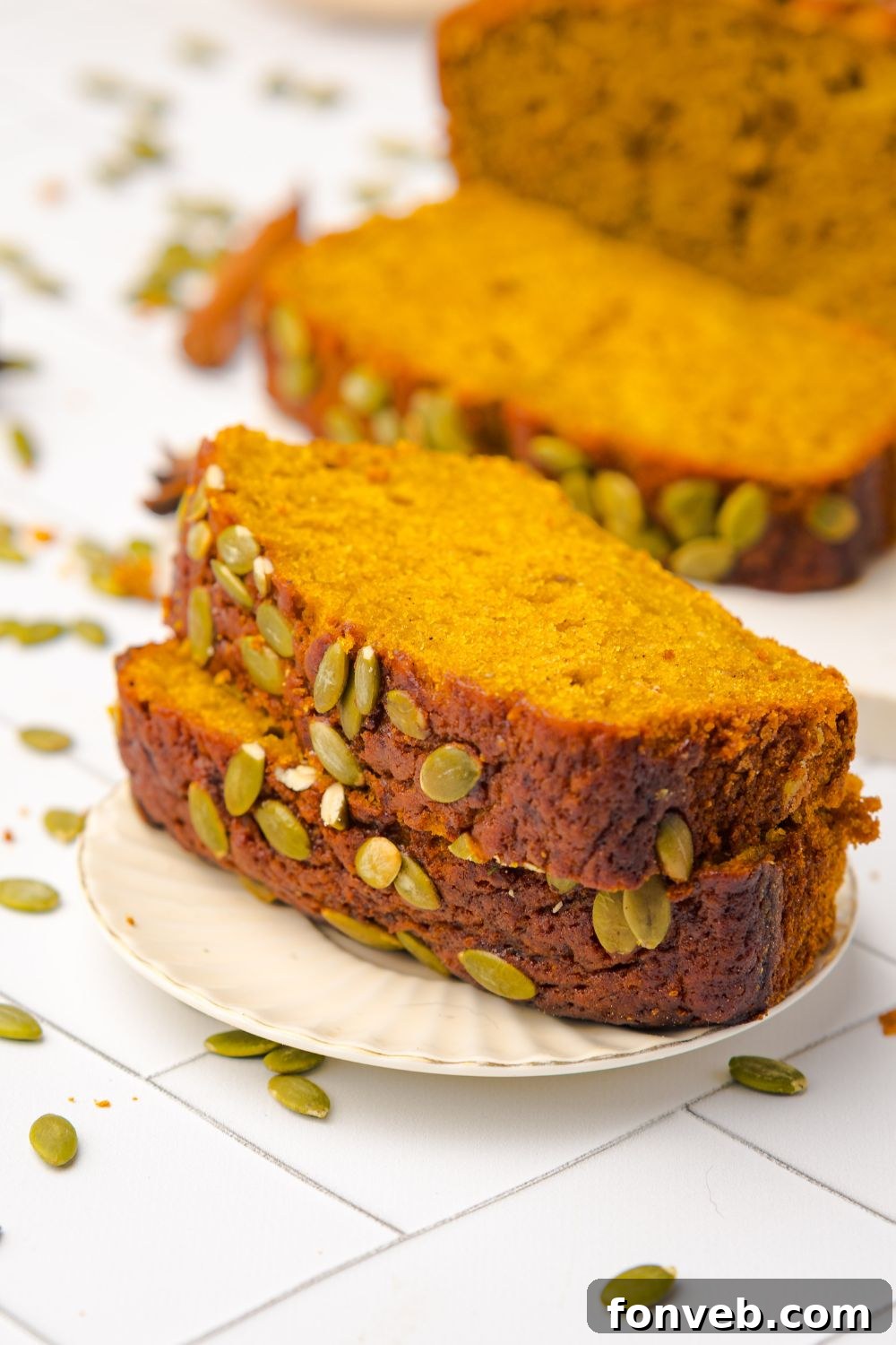 slices of Starbucks Pumpkin Bread on a white plate with more bread behind it on the white table and seeds scattered around the table 