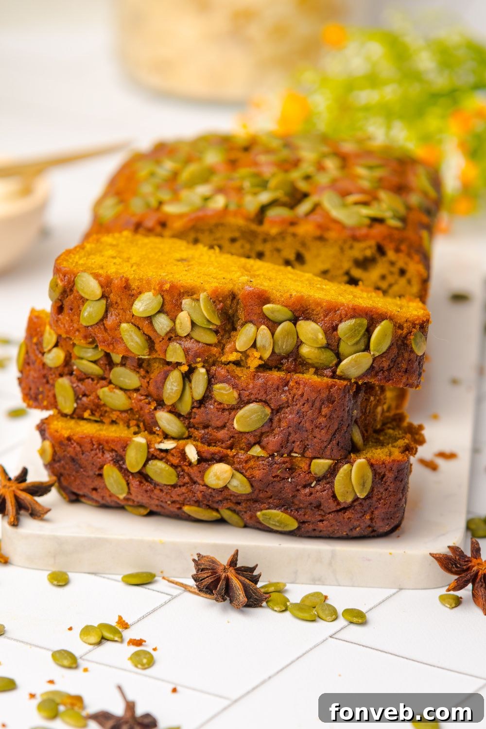 three slices of Starbucks Pumpkin Bread stacked on top of one another, with the rest of the pumpkin loaf behind it on a white table 