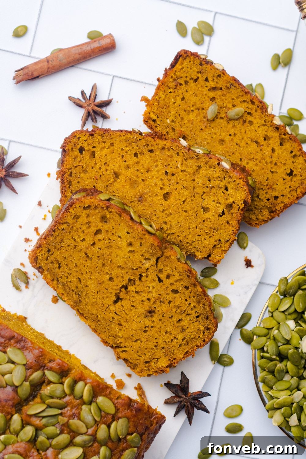 slices of Starbucks Pumpkin Bread placed on table and the rest of the remaining loaf setting on a white table with pumpkin seeds in a glass bowl to the side 