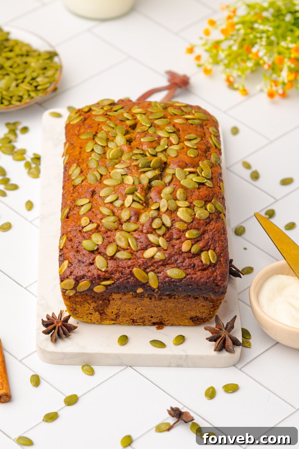 whole loaf of Starbucks Pumpkin Bread on a cutting board on table with seeds and cinnamon sticks scattered around table 