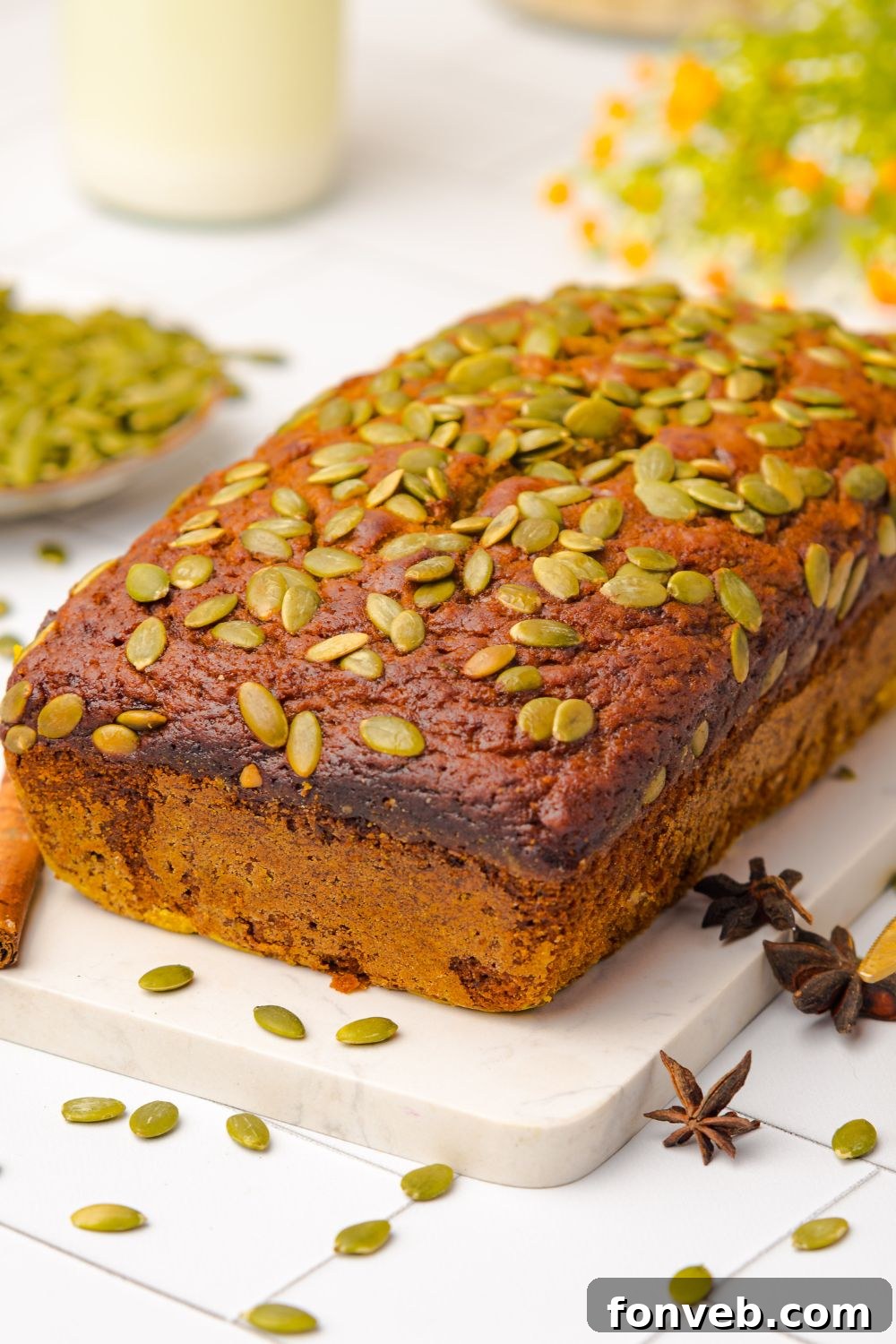 Starbucks Pumpkin Bread loaf sitting on a white marble cutting board on a white table. To the side is a bowl of seeds that is scattered around the table 