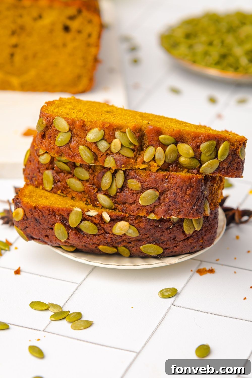 Starbucks Pumpkin Bread stacked on a plate with pumpkin seeds on top of bread and in a bowl to the side 
