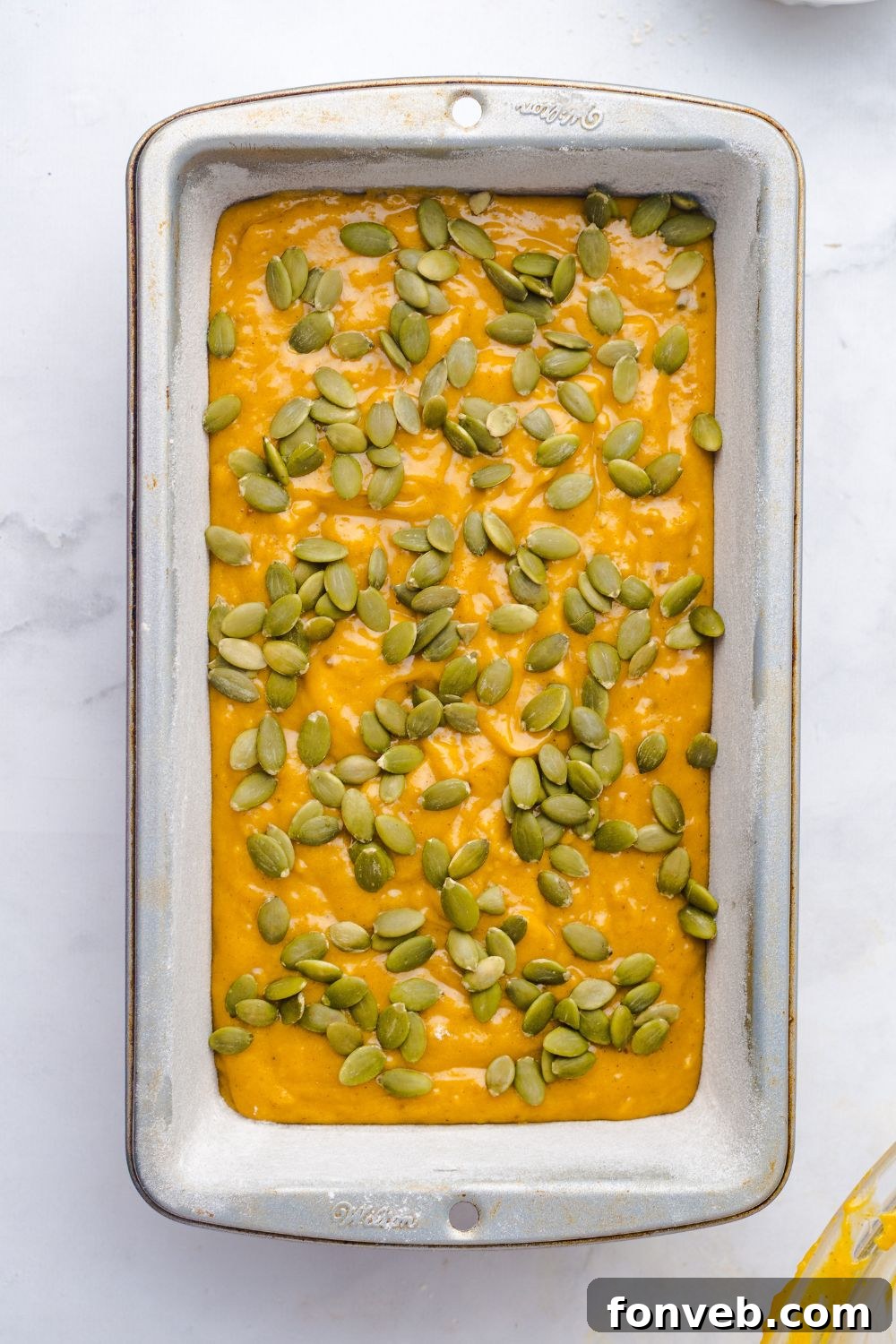 Starbucks Pumpkin Bread batter in a loaf pan on table topped with pumpkin seeds 