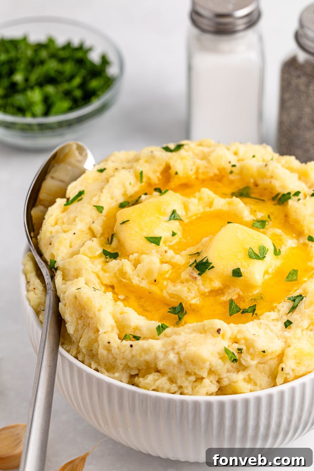 Effortless Creamy Garlic Mashed Potatoes 15 a white bowl sitting on table full of thick and creamy Garlic Mashed Potatoes with a spoon on its side wedged into the bowl