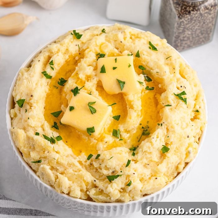 Effortless Creamy Garlic Mashed Potatoes 4 Garlic Mashed Potatoes in a white bowl sitting on a white table with salt and pepper shaker to the side of table