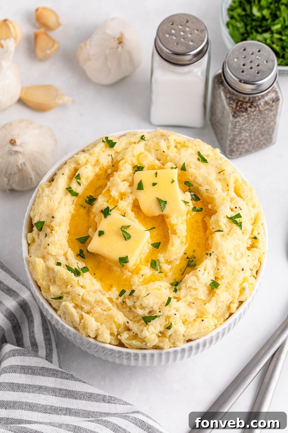 Effortless Creamy Garlic Mashed Potatoes 5 Garlic Mashed Potatoes placed in a white bowl with slabs of butter on top and some parsley