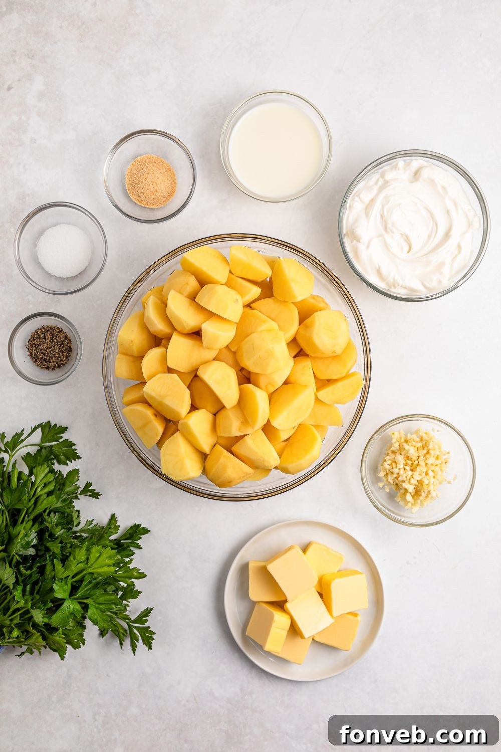 Effortless Creamy Garlic Mashed Potatoes 6 all the ingredients for Garlic Mashed Potatoes on a white table in small single serve bowls and a bundle of parsley to the side