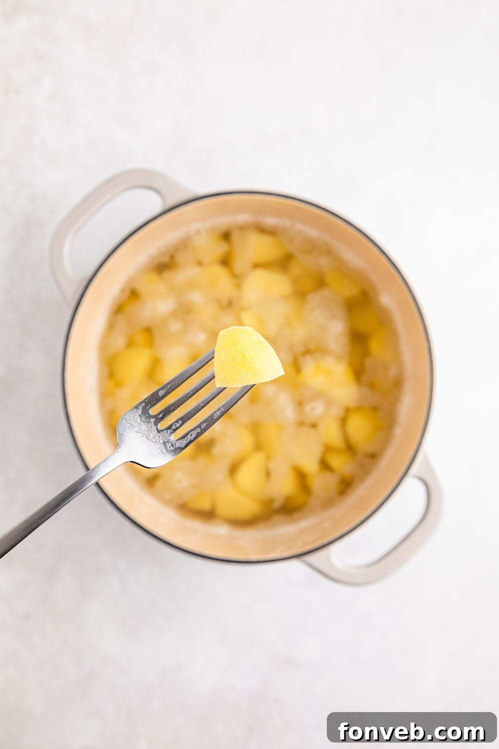 Effortless Creamy Garlic Mashed Potatoes 8 fork holding a potato above a pot full of potatoes and water on table