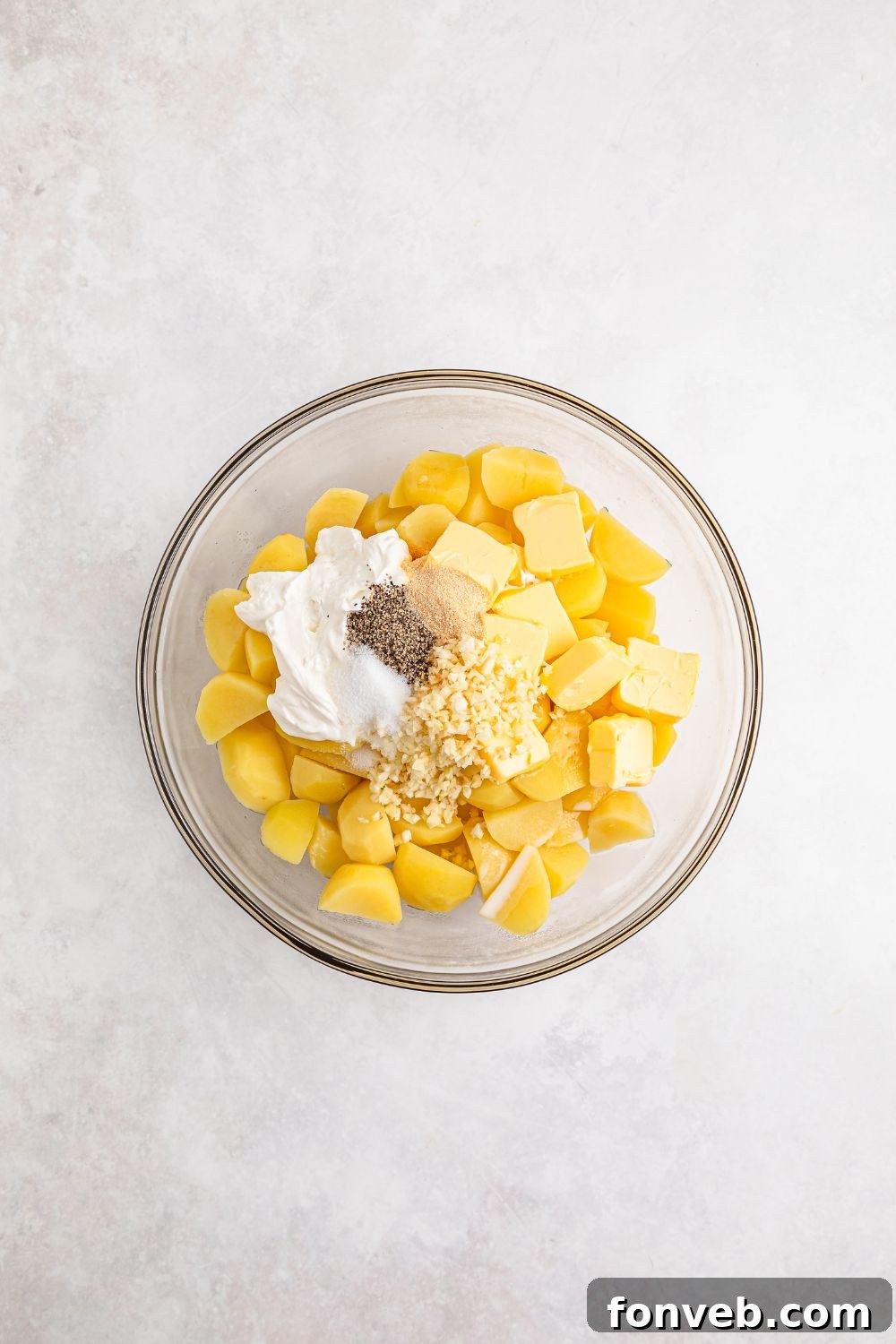 Effortless Creamy Garlic Mashed Potatoes 9 cooked potatoes, sour cream, spices and more in a glass bowl on white table