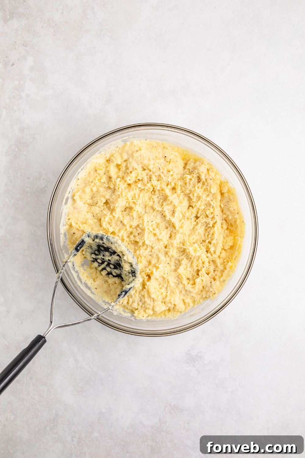 Effortless Creamy Garlic Mashed Potatoes 10 mashed potatoes in a glass bowl with a potato masher placed in the bowl