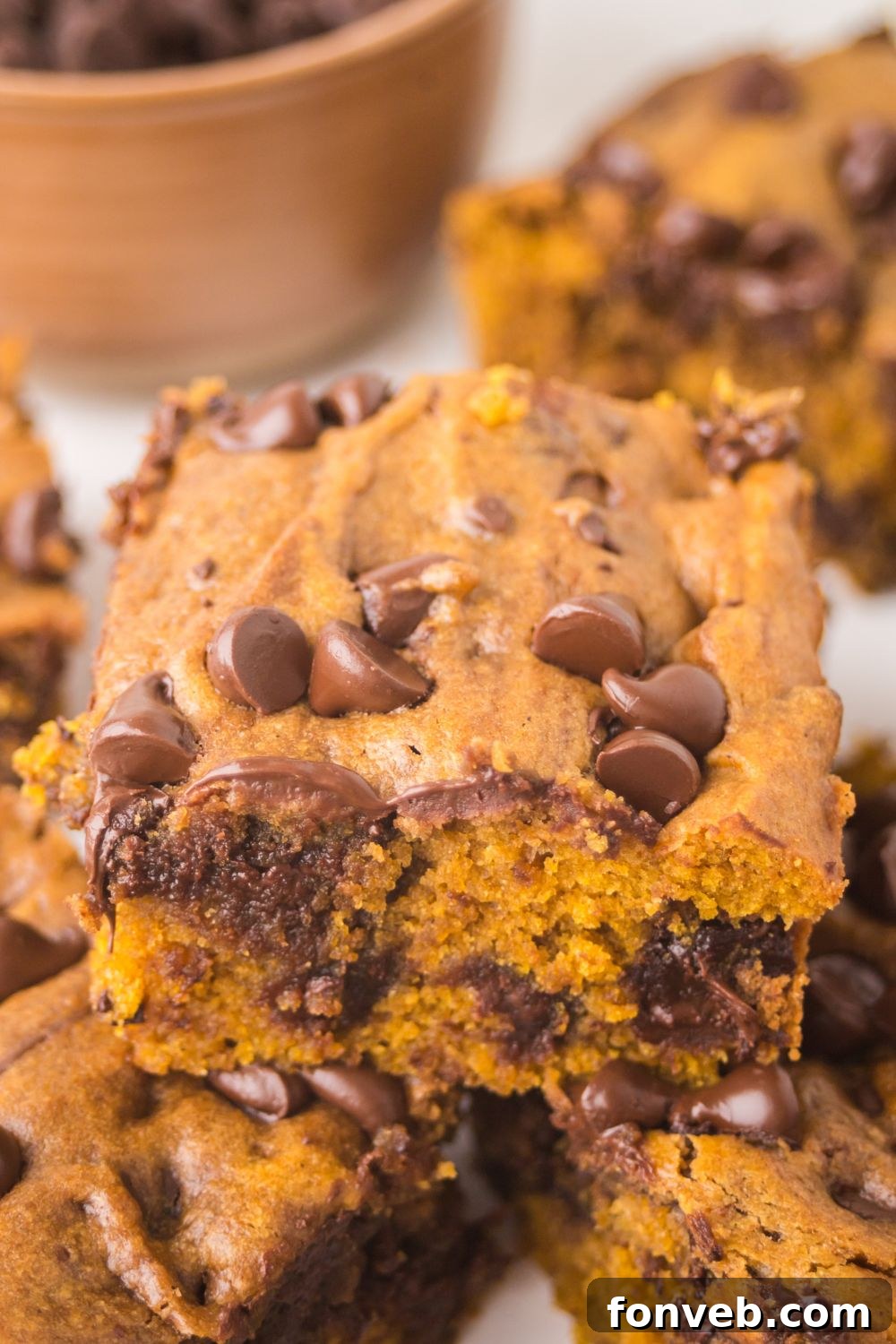 Brown Butter Pumpkin Chocolate Chip Bars stacked on top of one another on a white platter sitting on the table 