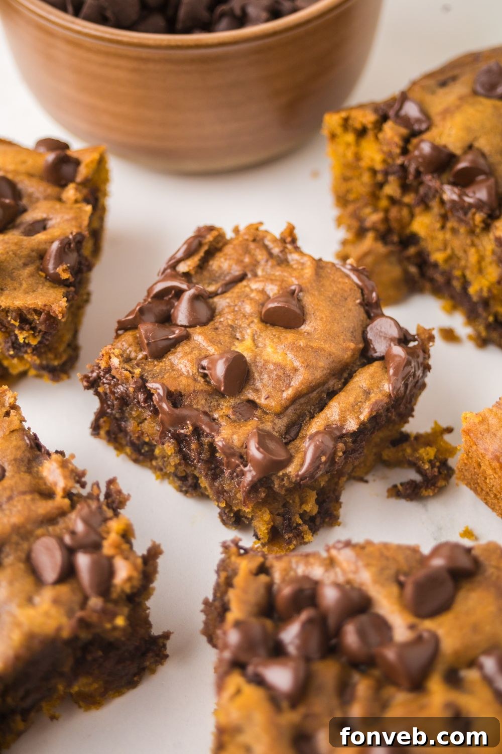 Brown Butter Pumpkin Chocolate Chip Bars cut into squares and placed around the table with a bowl of chocolate chips behind it on table 