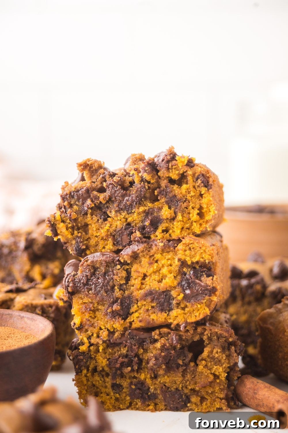 Brown Butter Pumpkin Chocolate Chip Bars stacked on top of one another with more bars placed around the white table 