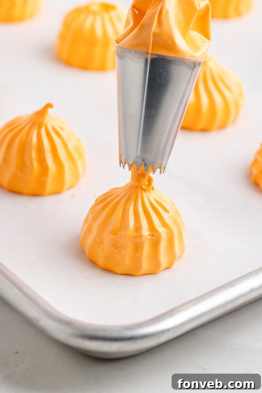 piping out a Pumpkin Meringue cookie shape onto a metal baking sheet with parchment paper 